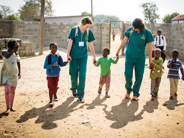 Nursing students walking hand in hand with children in another country